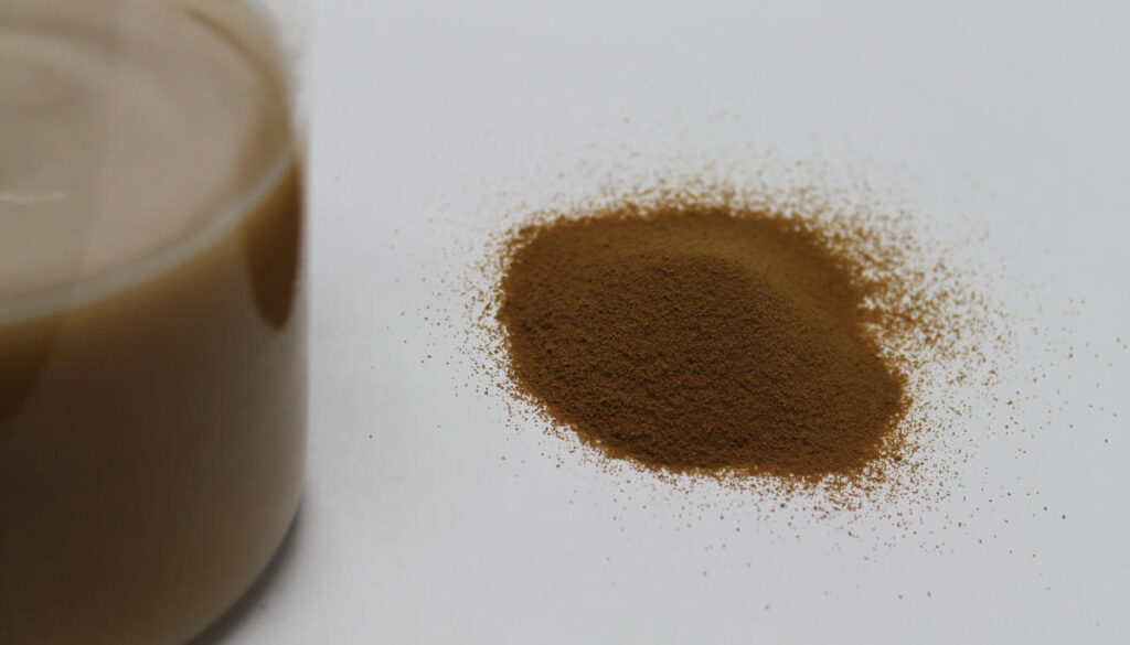 Bti-Pulver ist zu einem Häufchen angesammelt, daneben steht ein Becherglas in dem Bti-Pulver in Wasser gelöst wurde.