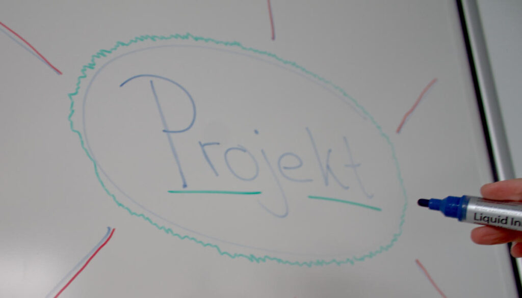 Auf einem Whiteboard steht das Wort Projekt.