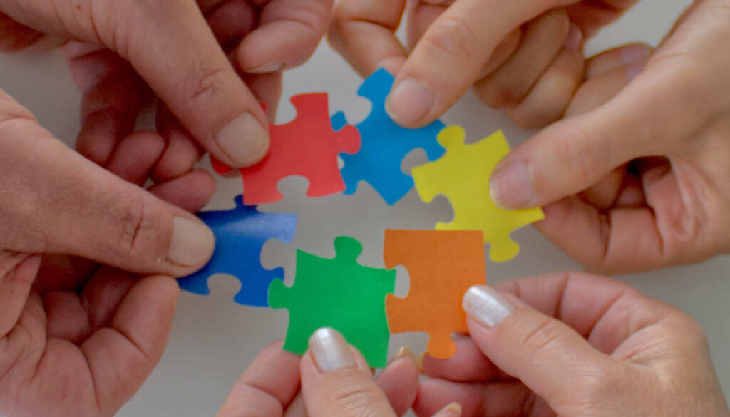 Hände halten Puzzleteile aneinander.