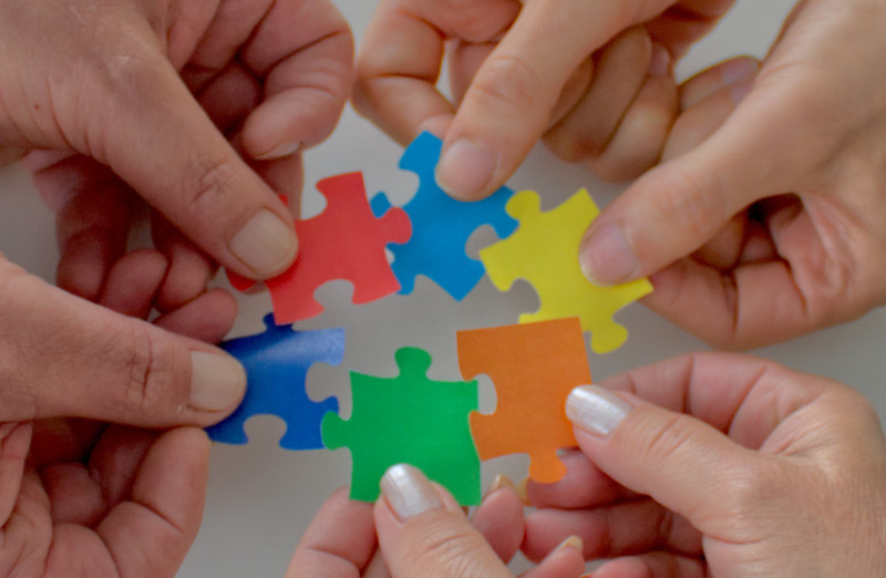 Hände halten Puzzleteile aneinander.
